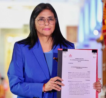 Una mujer con cabello oscuro y gafas, vestida con un blazer azul, sostiene un documento con texto rojo y negro que dice 'LEY DE AMNISTÍA'