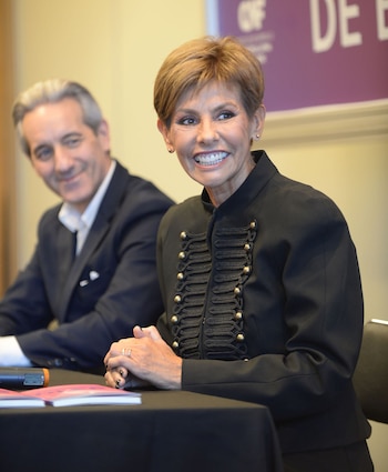 Primer plano de Stella Maris Cuevas, una mujer de cabello castaño corto, sonriendo y vistiendo una chaqueta negra con botones dorados, con un hombre borroso detrás