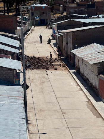 Vista aérea de una calle con casas bajas, un poste de luz, cables, varias personas y un montón de escombros de ladrillo y tierra en el centro