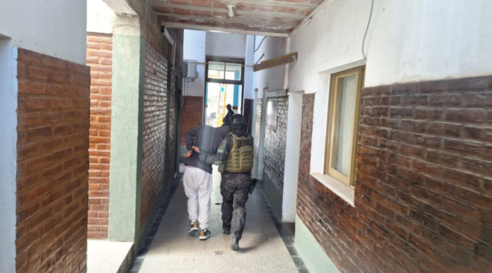 Otro de los detenidos es escoltado por un agente de la FPA en un corredor tras los allanamientos contra una banda narco en Villa Dolores, Córdoba (Ministerio Público de Córdoba)
