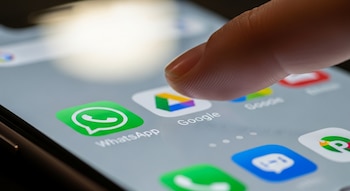 Primer plano de un dedo tocando la pantalla de un smartphone, con los iconos de WhatsApp y Google Drive claramente visibles en primer plano.