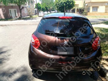 Parte trasera de un automóvil Peugeot 208 color marrón oscuro estacionado en una calle, con casas y árboles de fondo