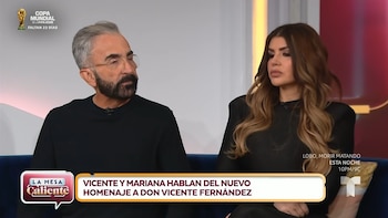 Vicente Fernández Jr, un hombre de barba gris y gafas, y Mariana González, una mujer de cabello largo ondulado, sentados en un sofá azul en un set de televisión