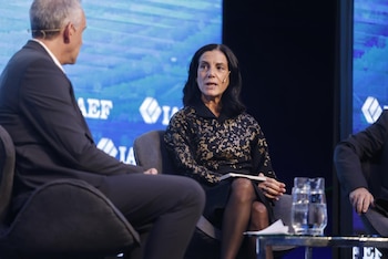 Azucena Arbeleche, con cabello oscuro y blusa negra con detalles dorados, sentada en un panel de discusión, hablando. Un hombre se sienta a su izquierda