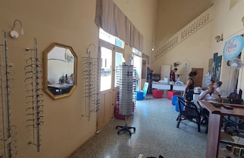 Interior de una óptica con exhibidores de anteojos en las paredes, un espejo octogonal, exhibidores giratorios y varias personas sentadas