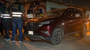 Varios policías con chalecos reflectantes junto a una camioneta roja estacionada de noche frente a una pared de ladrillo.