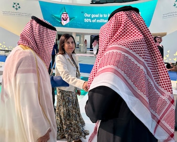 Margarita Robles saluda a dos hombres con vestimenta tradicional saudí frente a una pantalla con un retrato de Mohammed bin Salman