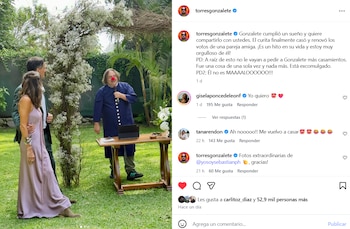 Un hombre con túnica azul y nariz de payaso roja oficia una ceremonia, una pareja está de pie a su izquierda, un jardín con arco floral y una mesa de madera