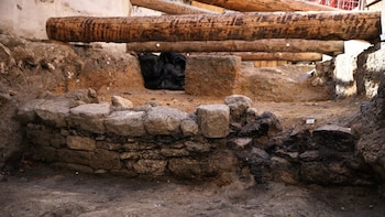 Muro bajo de piedras superpuestas sobre suelo de tierra en una excavación subterránea cubierta por vigas de madera de gran tamaño