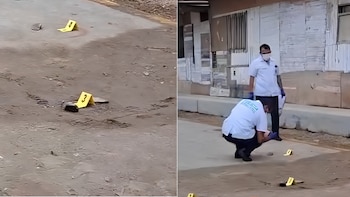 Dos policías examinan un terreno con marcadores de evidencia amarillos numerados. Uno está de pie y otro agachado, cerca de una edificación