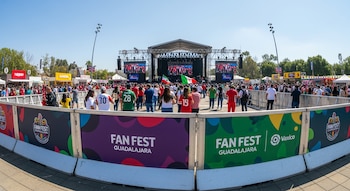 Vista panorámica de un Fan Fest en Guadalajara con una gran multitud de personas frente a un escenario con pantallas y vallas de seguridad de colores en primer plano.