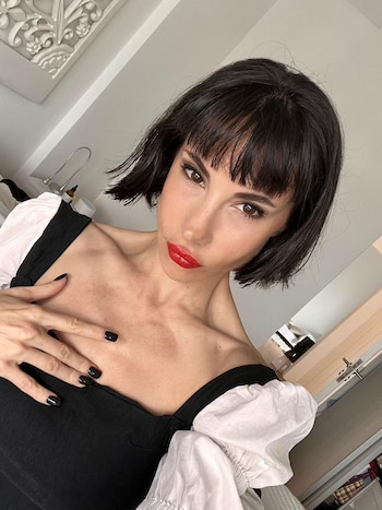 Retrato de Magui Bravi, mujer con cabello oscuro corto y flequillo, labios rojos y uñas negras, vistiendo una blusa negra con mangas blancas abullonadas