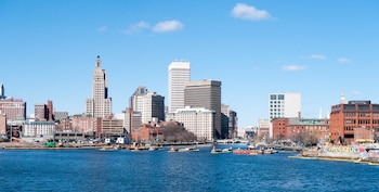 Horizonte de Providence con edificios variados, un río con barcazas de trabajo y la orilla con construcciones y grafitis bajo un cielo azul
