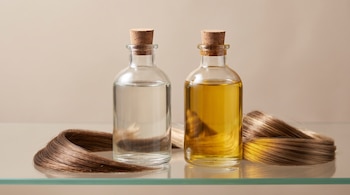 Dos frascos de vidrio con tapón de corcho, uno transparente y otro con líquido dorado, junto a mechones de cabello sobre un estante.