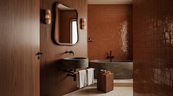 Un baño moderno con paredes de madera oscura y azulejos terracota. Incluye un lavabo de piedra, bañera a juego, espejo irregular y toallas blancas.