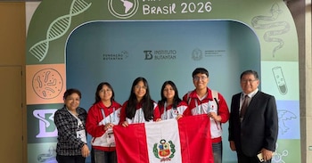 Cuatro estudiantes con casacas rojas sostienen la bandera peruana junto a dos adultos ante un panel decorado con la frase Brasil 2026