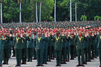 Una multitud de militares con uniformes verdes, boinas rojas y medallas amarillas, con la mano derecha levantada