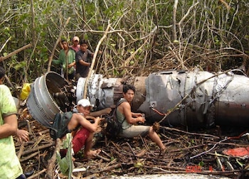 Varios hombres permanecen junto a los restos metálicos del motor de un avión rodeado de vegetación densa y ramas