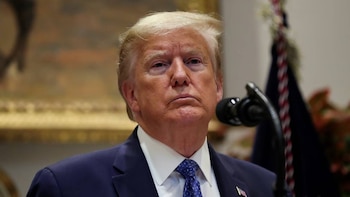 Close do presidente dos EUA, Donald Trump, vestindo terno azul e gravata azul, olhando para cima, com um microfone próximo