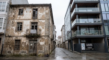 Edificio antiguo con cartel "se vende a reformar" frente a edificio moderno de cristal con balcones y cartel "Luxury Residences".