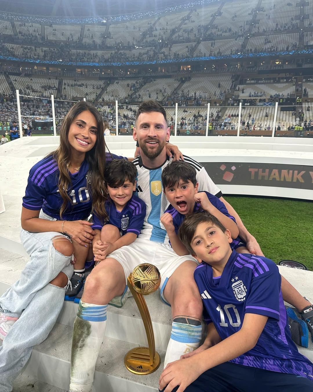 Lionel Messi celebró su victoria en la Copa Mundial con Antonela Roccuzzo y sus hijos, posando con el Balón de Oro en el campo de juego de un estadio.