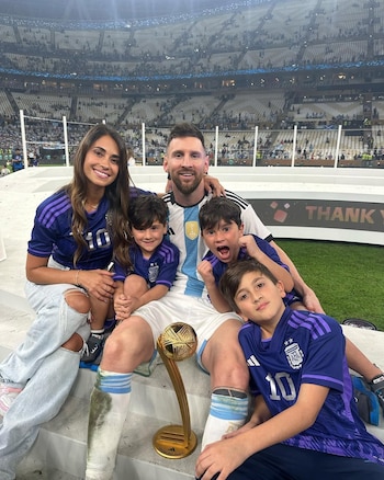 Lionel Messi, Antonela Roccuzzo y sus tres hijos posan sonrientes en el campo de un estadio, Messi con el Balón de Oro