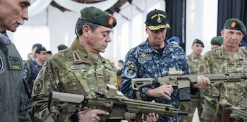 Militares con uniformes de camuflaje y boinas sostienen y examinan fusiles en un recinto cerrado junto a otros oficiales