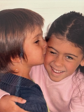 Un niño besa en la mejilla a una niña sonriente vestida de rosa que lo abraza