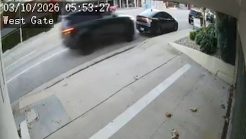 Captura de cámara de seguridad que muestra una calle con vehículos oscuros, una acera y texto digital con la fecha y las palabras West Gate