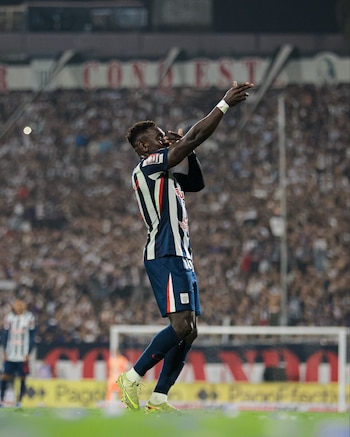 Un futbolista, Eryc Castillo, con uniforme azul y blanco a rayas, celebra un gol con los brazos en alto frente a una multitud borrosa en el estadio