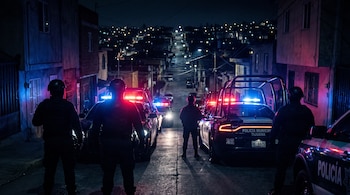 Agentes con casco y patrullas con luces rojas y azules encendidas en una calle inclinada durante la noche.