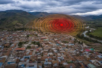 Vista aérea de una ciudad de casas con techos de teja, montañas verdes al fondo, un río y círculos rojos concéntricos sobre las colinas.