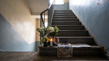 Escalera de metal en el interior de un edificio, con un jarrón de flores, una vela encendida, una fotografía enmarcada, una camiseta y un cuaderno abierto.