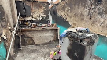 Interior de una vivienda con paredes, techo y suelo de color negro por el hollín, con una encimera de cocina y una lavadora dañadas por el fuego