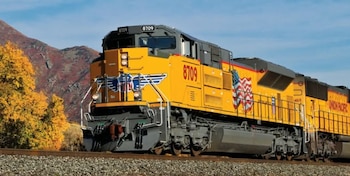 Una locomotora de color amarillo con el número 8709 y el logo de Union Pacific avanza sobre rieles en un paisaje montañoso