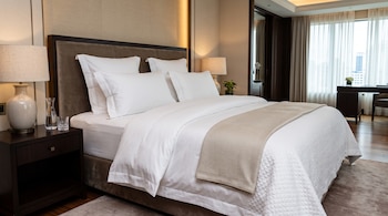 Una cama doble hecha con sábanas y almohadas blancas junto a dos mesas de noche con lámparas y un escritorio.