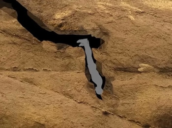 Una ilustración digital muestra una grieta oscura y profunda en una formación rocosa de color marrón, con una figura gris descendiendo por el paso