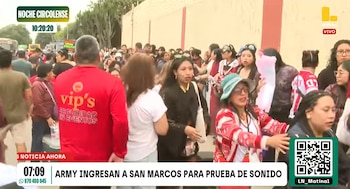 Una multitud de personas camina junto a un muro exterior, acompañada por personal de seguridad con camiseta roja
