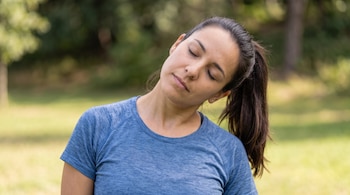 Primer plano de una mujer con camiseta azul que inclina la cabeza hacia un lado con los ojos cerrados en un entorno verde.