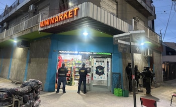 Varios agentes de policía permanecen en la entrada de un minimarket ubicado en una esquina con carteles callejeros en Morón