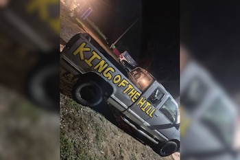 Camioneta gris de perfil con el texto King of the Hill pintado en amarillo sobre el lateral, fotografiada de noche sobre un terreno de tierra