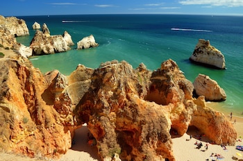 El mar se aprecia oscuro y se va aclarando a medida que se acerca a la playa. La playa está llena de formaciones geológicas parecidas a un acantilado en rocas, muy escarpado.