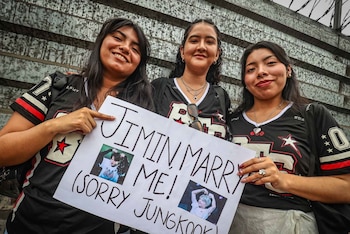 Tres jóvenes con camisetas negras sostienen un cartel blanco con la frase Jimin marry me