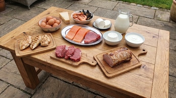 Mesa de madera con una diversa selección de alimentos ricos en proteínas: pollo, ternera, cerdo, atún, salmón, mariscos, huevos, quesos, leche y yogur.
