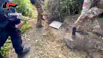 Dos agentes, uno con uniforme oscuro y otro camuflado, examinan un objeto blanco plano (Bedrock) y un cilindro oscuro (M-tree) en el suelo