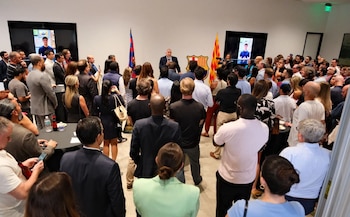 Un orador habla a una audiencia en un evento. Al fondo, el escudo del FC Barcelona, banderas y dos pantallas mostrando a un joven