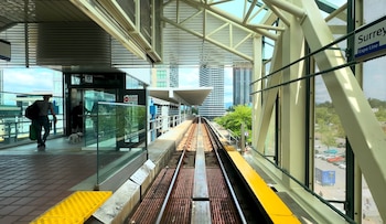 Imagen desde la plataforma de una estación del SkyTrain en Vancouver, con vías de tren en el centro, personas, estructura del techo y edificios altos