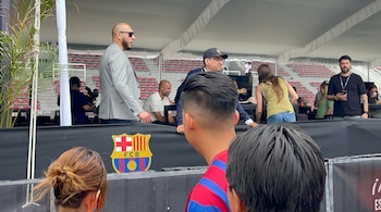 Vista parcial de un grupo de personas bajo una carpa con el escudo del FC Barcelona en primer plano y gradas vacías de estadio al fondo.