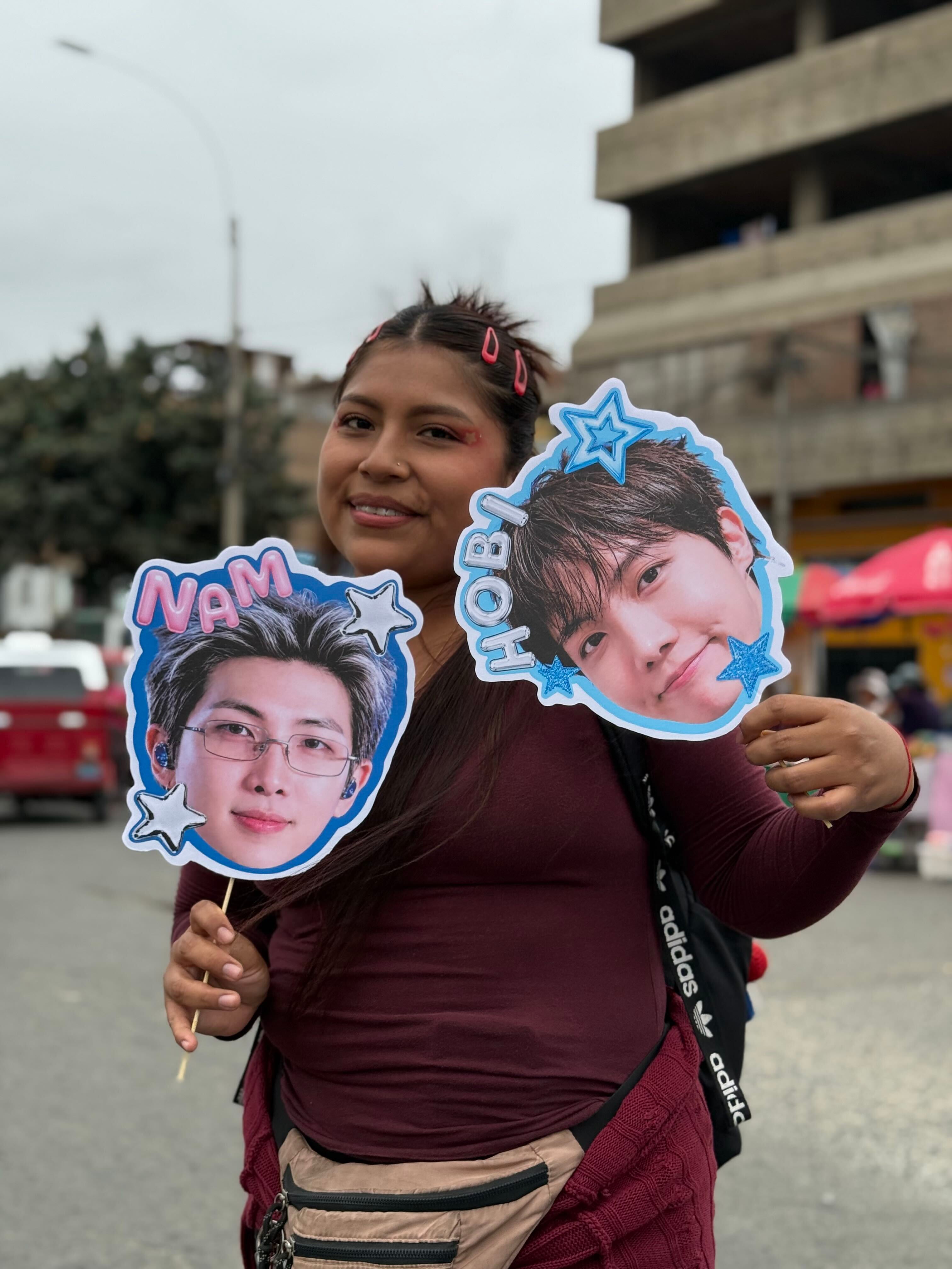 Una comerciante sostiene carteles con los rostros de integrantes del grupo BTS en las inmediaciones del Estadio San Marcos durante la venta de mercancía en Lima. (Paula Díaz)