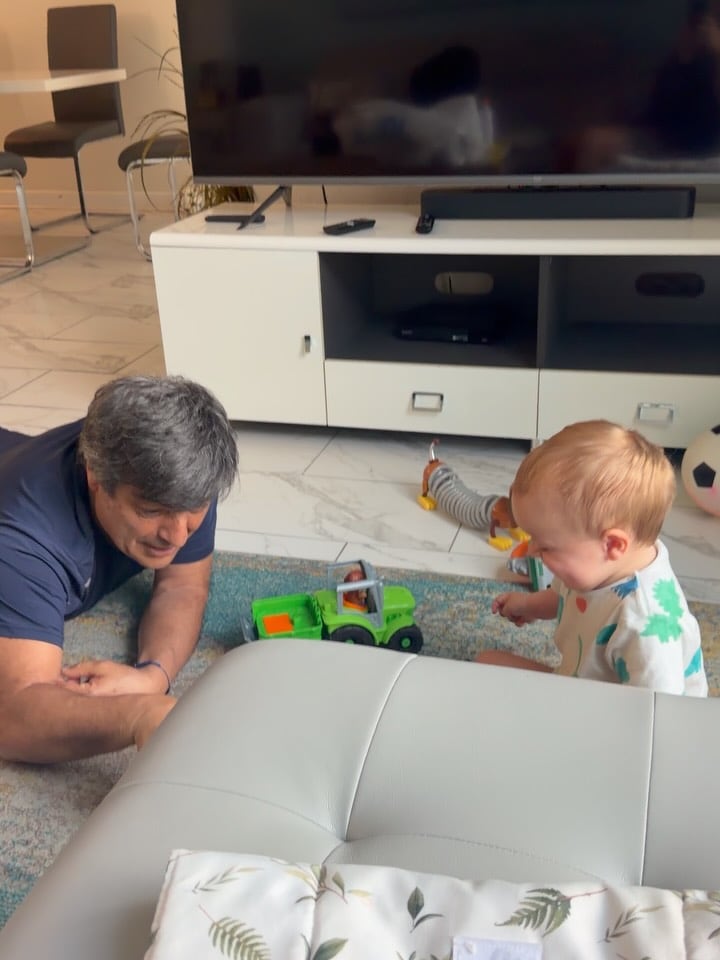 El pequeño Marco, hijo de Sol Pérez, juega en el suelo con un tractor de juguete en compañía de su abuelo.